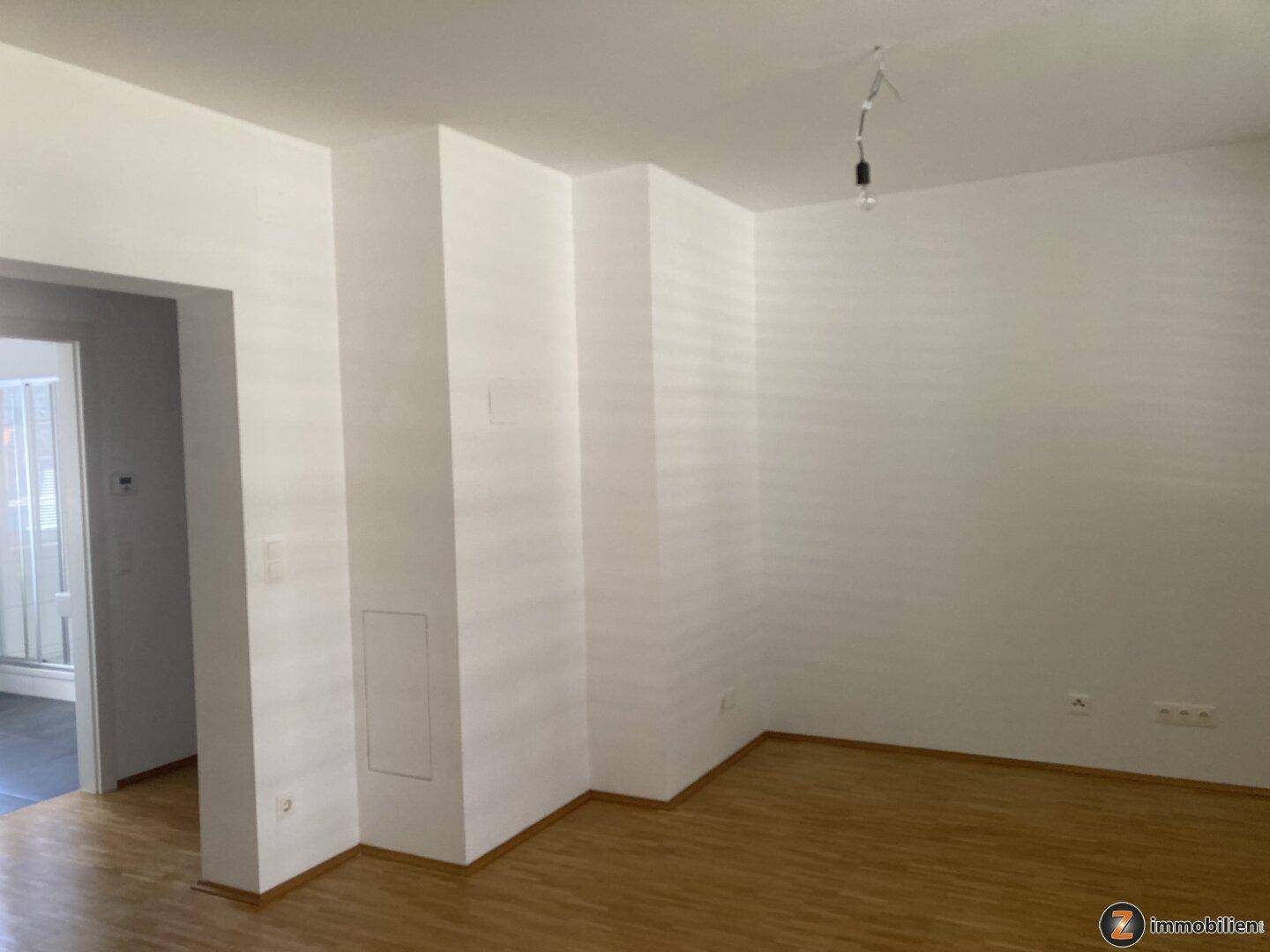 Geräumiges, helles Wohnzimmer mit Parkettboden und weißen Wänden, unmöbliert.