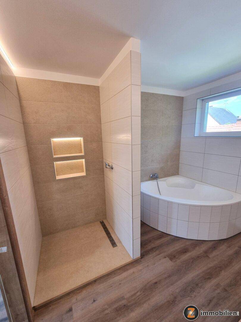 Gefliestes Badezimmer mit begehbarer Dusche, Eckbadewanne und integrierten Nischen.