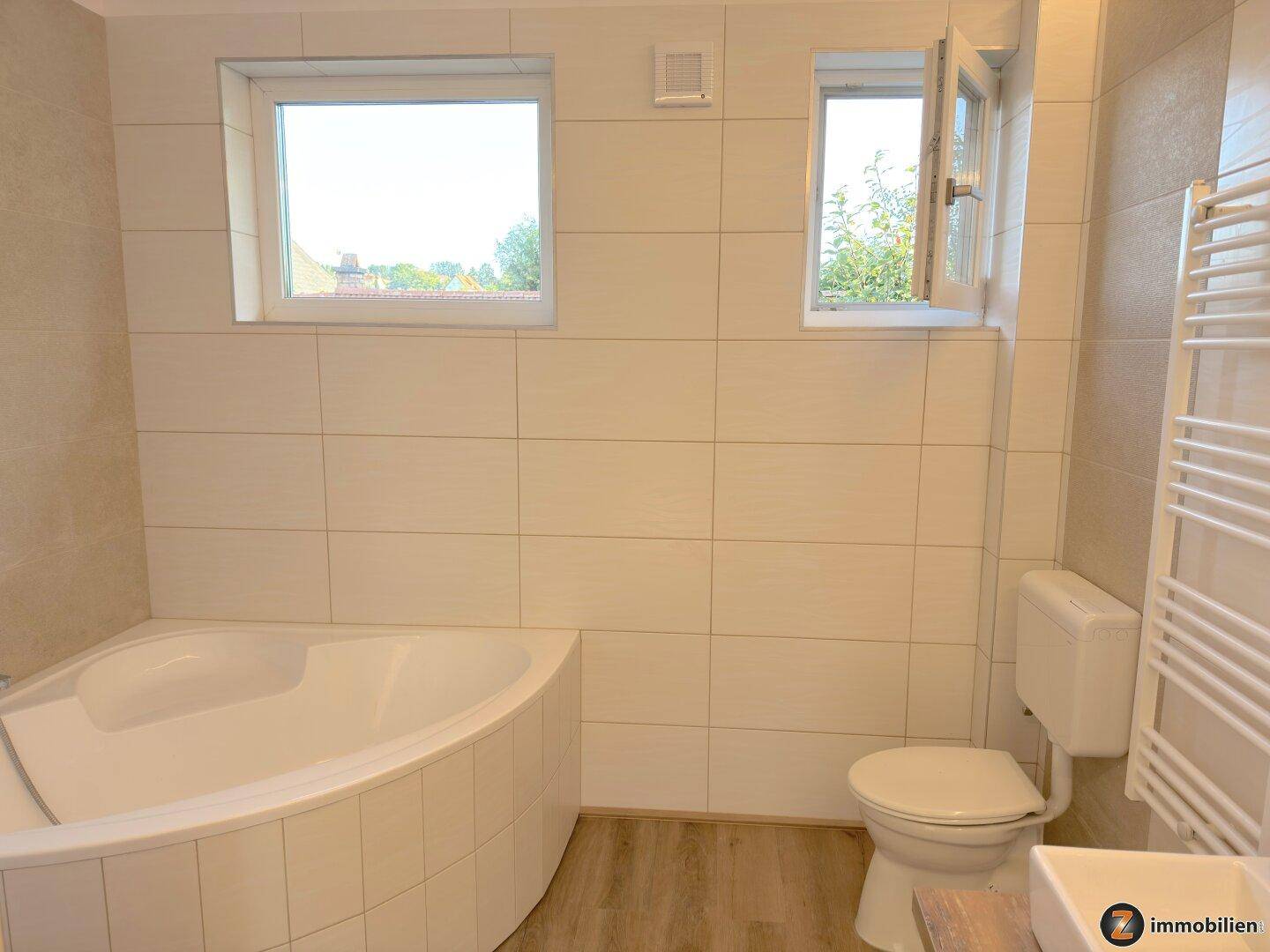 Modernes Badezimmer mit Eckbadewanne, WC und Fenster für natürliche Belüftung.