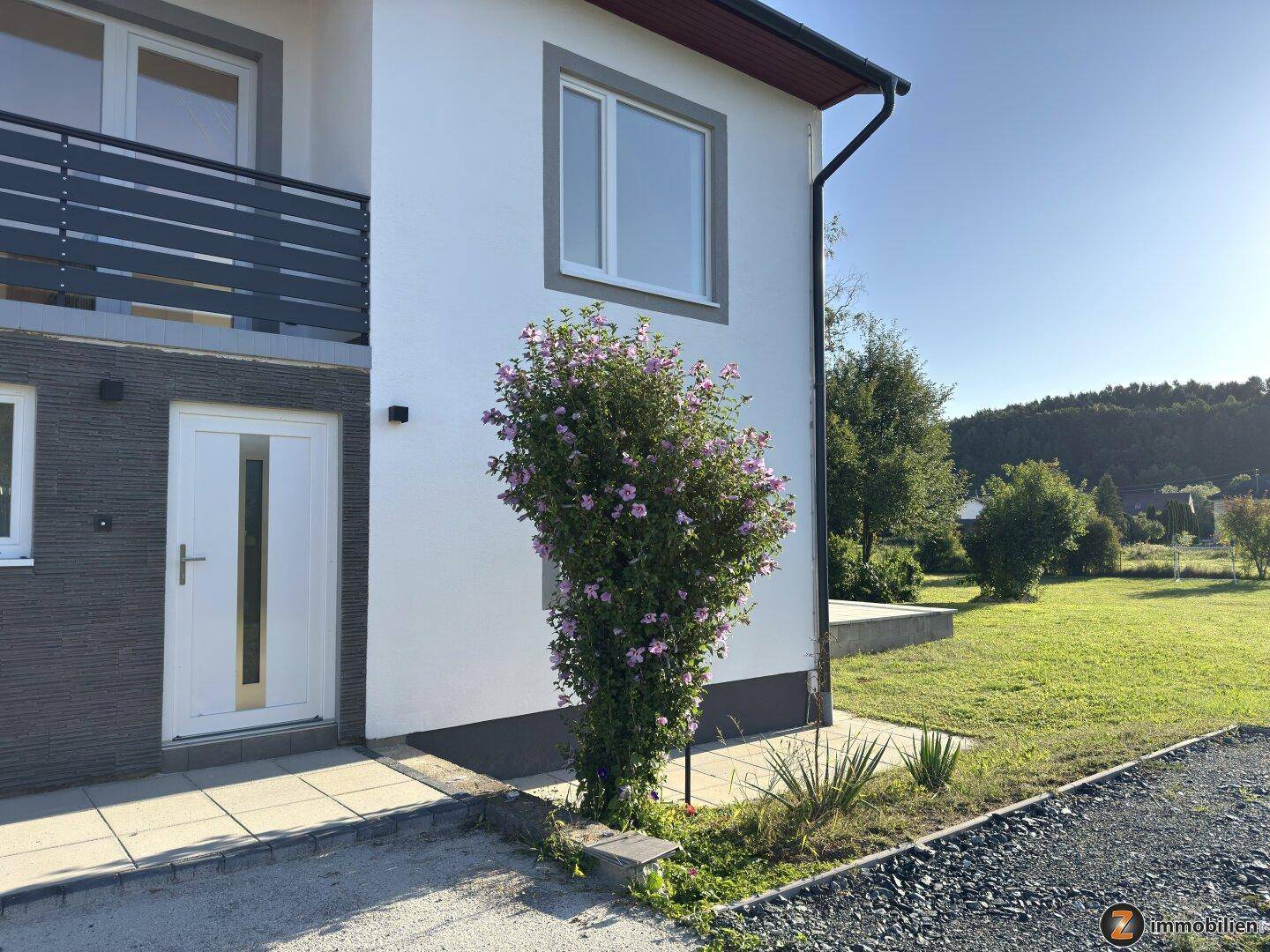 Seitenansicht des Hauses mit blühendem Strauch und Zugang zum Gartenbereich.