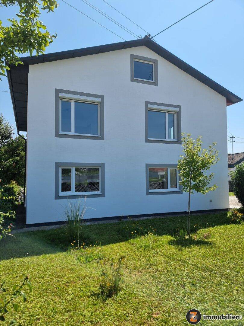 Freistehendes Einfamilienhaus mit weißer Fassade, grauen Akzenten und großem Garten.