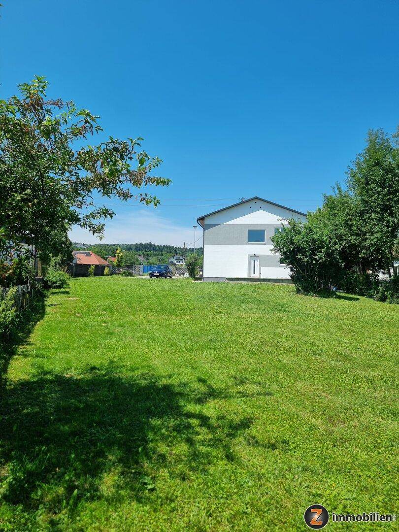 Weitläufiger grüner Gartenbereich mit dem Haus im Hintergrund unter blauem Himmel.
