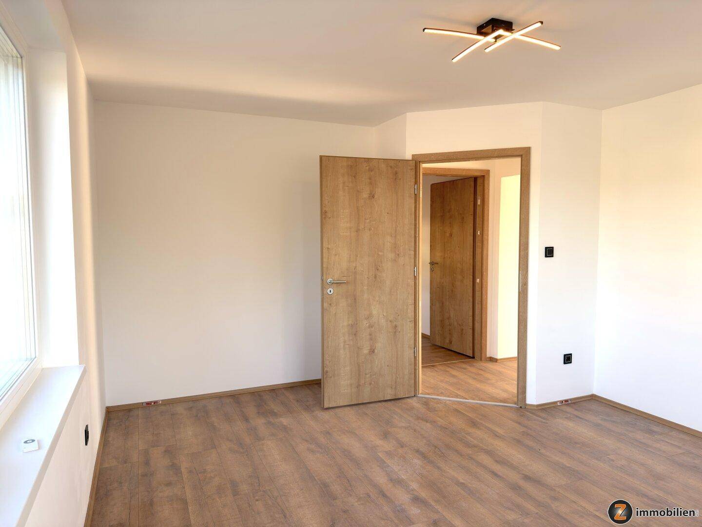 Helles Schlafzimmer mit Holztüren und Laminatboden, bietet Zugang zu weiteren Räumen.