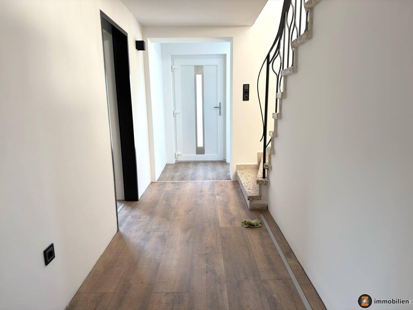 Eingangsbereich mit moderner Haustür und hellem Laminatboden, führt ins Innere des Hauses.