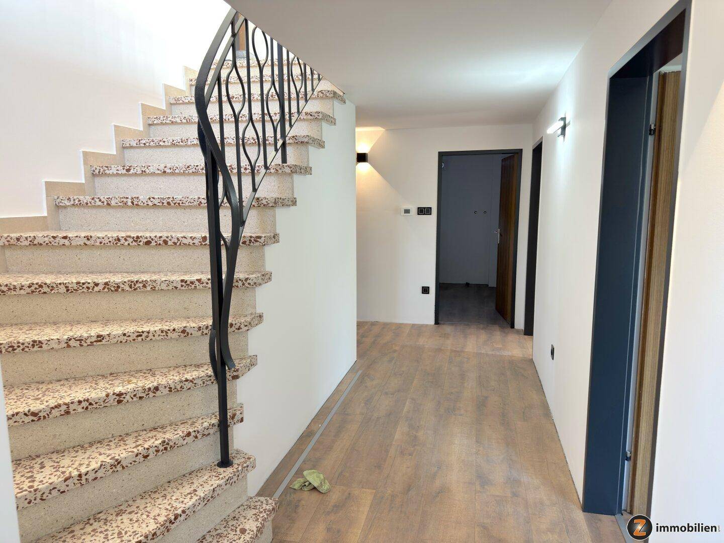 Heller Flur mit eleganter Treppe und schmiedeeisernem Geländer, führt zu den oberen Etagen.