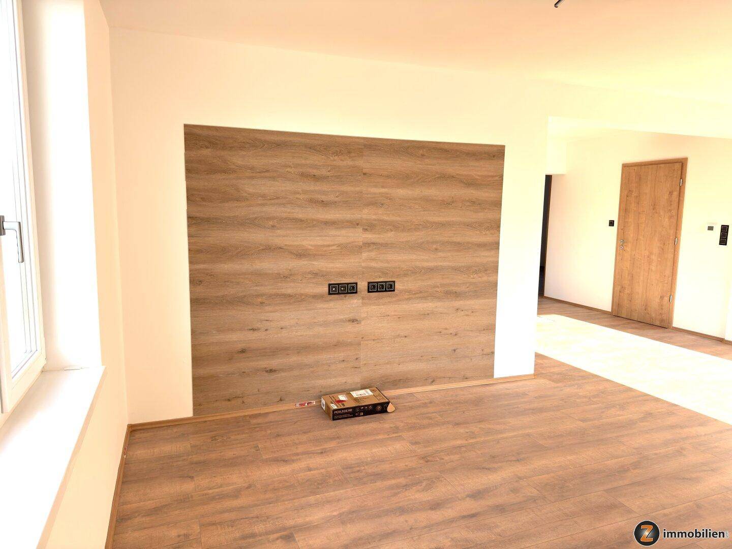 Moderner Wohnbereich mit einer Akzentwand in Holzoptik und vorbereiteten Anschlüssen.