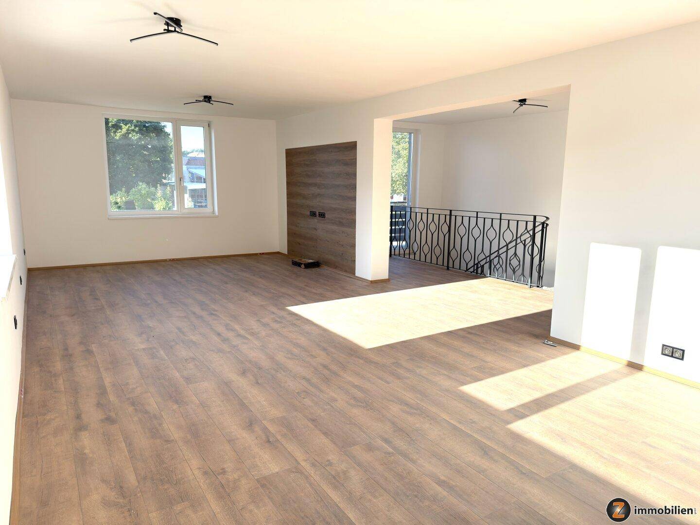 Geräumiges Wohnzimmer mit neuem Laminatboden, großen Fenstern und Blick ins Grüne.