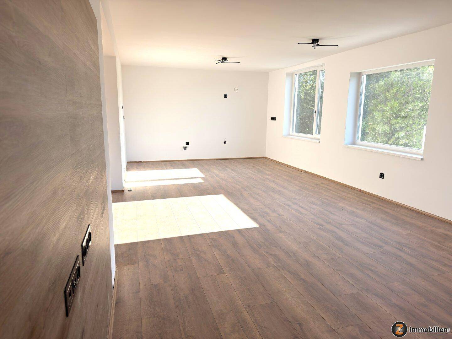 Helles Wohnzimmer mit Laminatboden und viel Tageslicht durch mehrere Fenster.