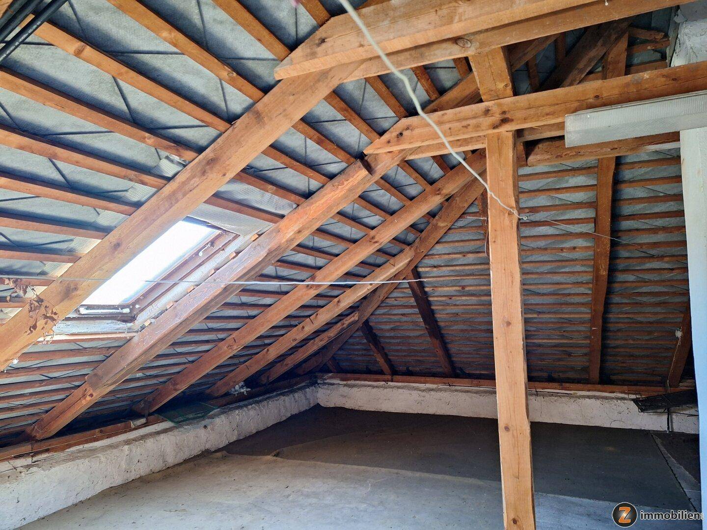 Unausgebauter Dachboden mit sichtbaren Holzbalken und einem Dachfenster für Tageslicht.