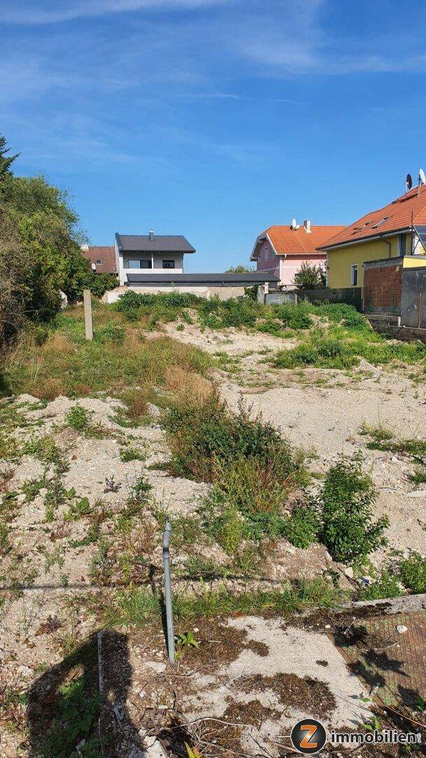 Unbebautes Grundstück mit Blick auf umliegende Wohnhäuser unter blauem Himmel.