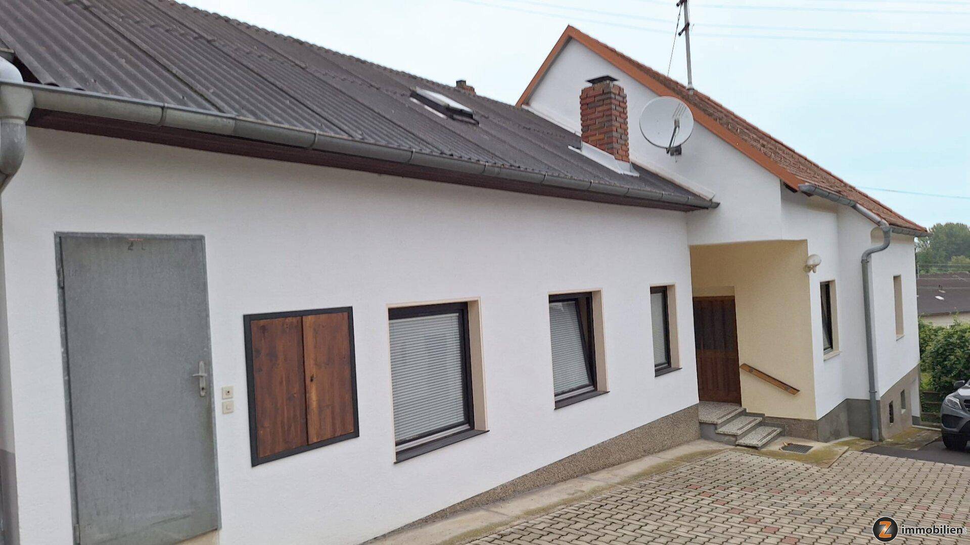 Seitenansicht des Hauses mit Satteldach, weißer Fassade und Satellitenschüssel.