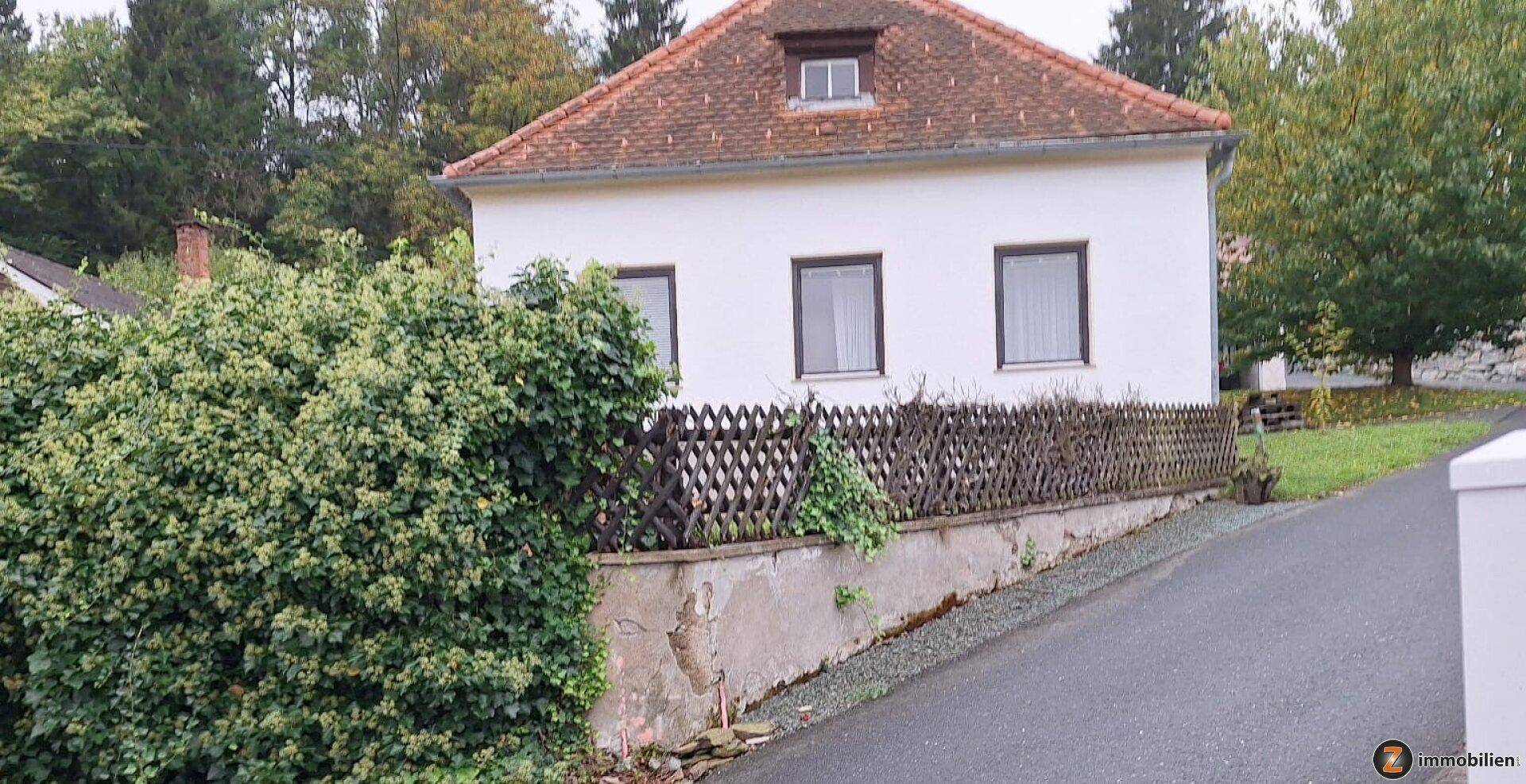 Freistehendes Haus mit Ziegeldach, umgeben von Hecken und einem Holzzaun.
