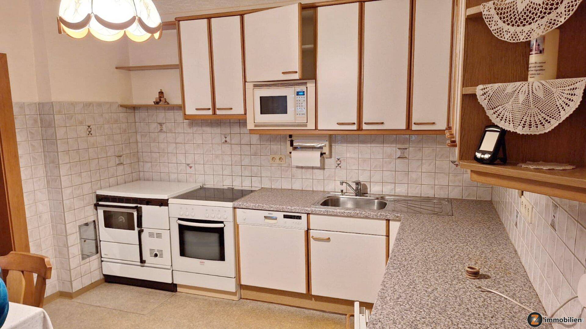 Funktionale Küche mit weißen Schränken, integrierter Mikrowelle und gefliestem Spritzschutz.