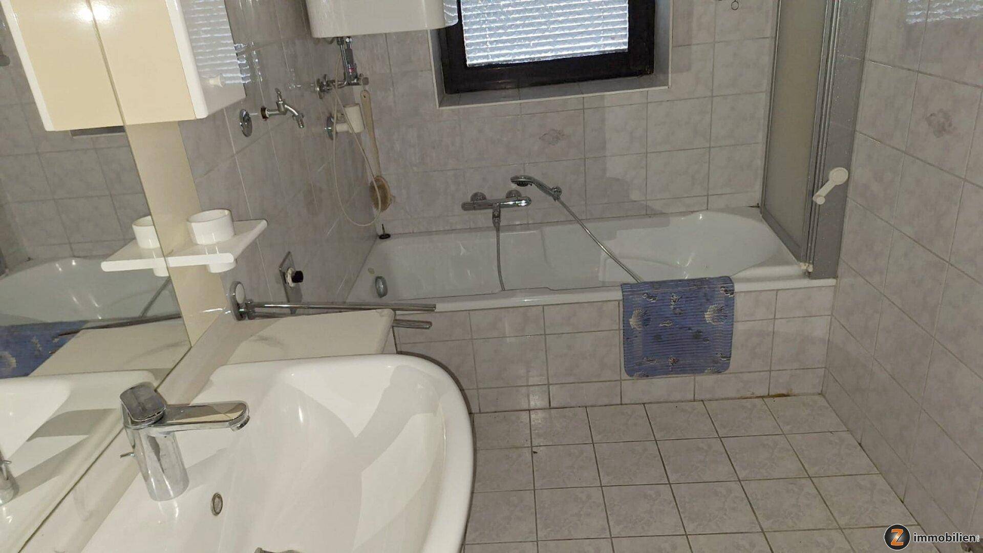 Badezimmer mit Badewanne, Duschabtrennung, Waschbecken und hellen Fliesen an Wänden und Boden.