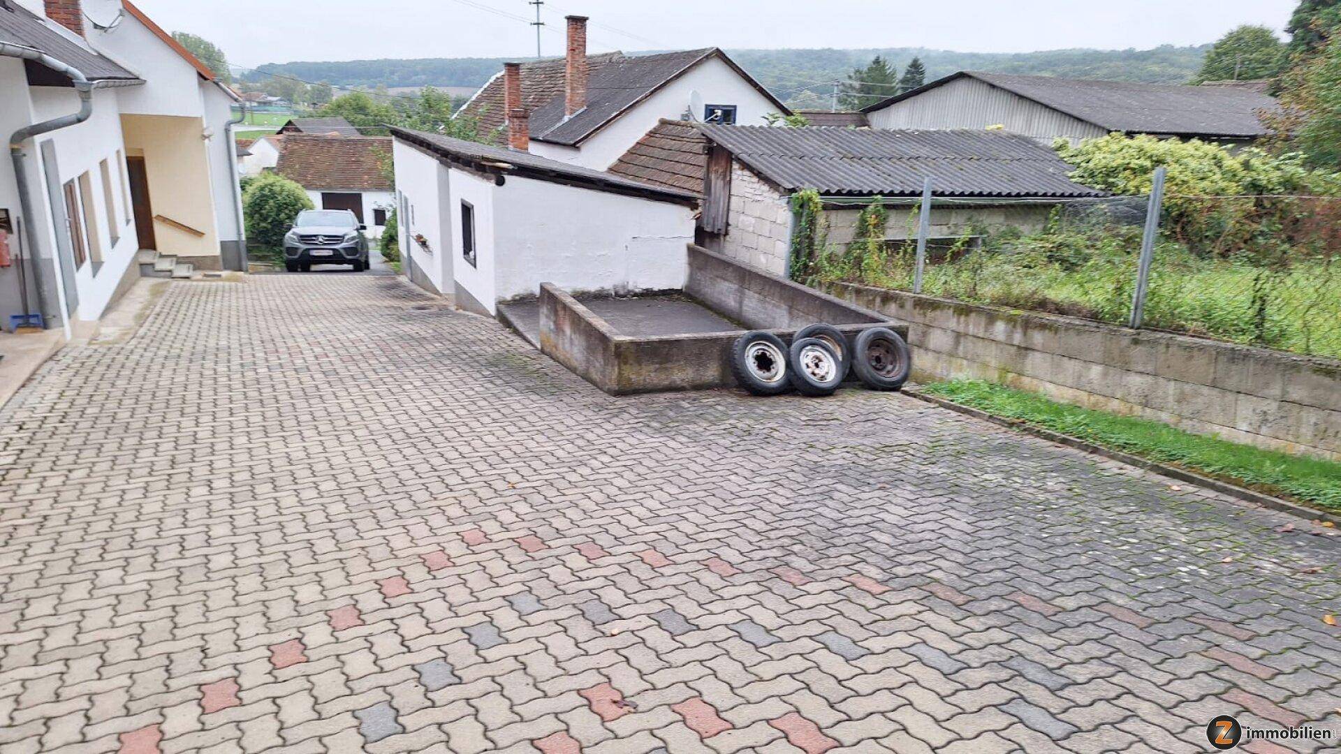 Gepflasterter Hofbereich mit mehreren Gebäuden und einer Betonrampe mit Reifen.