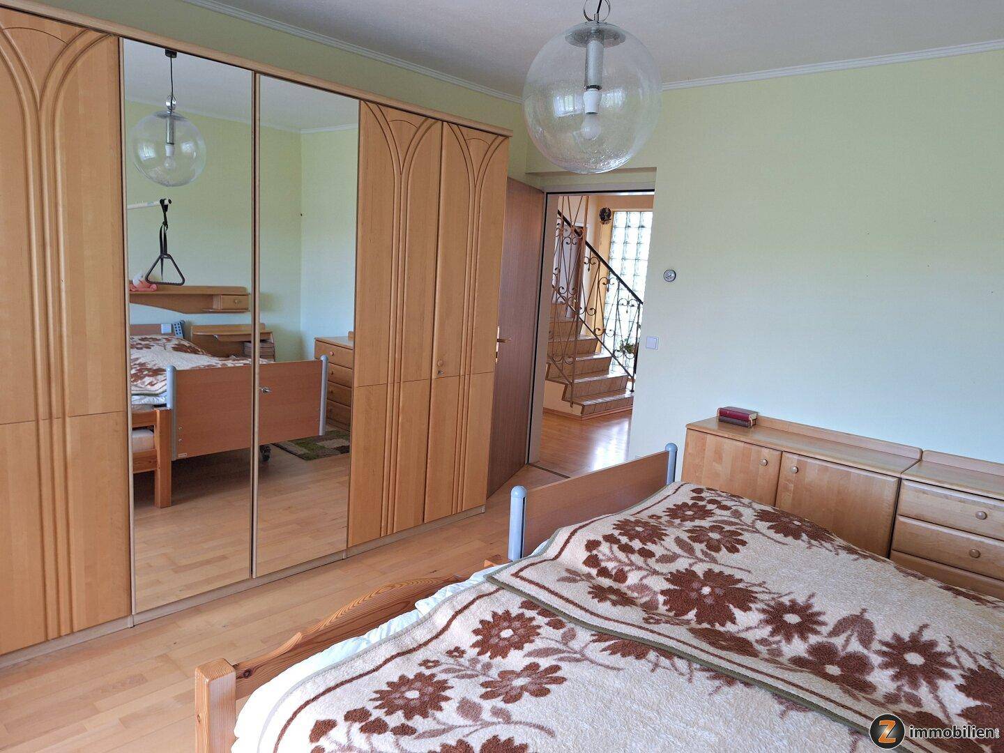 Schlafzimmer mit Doppelbett, Spiegelschrank und hellem Holzfußboden.