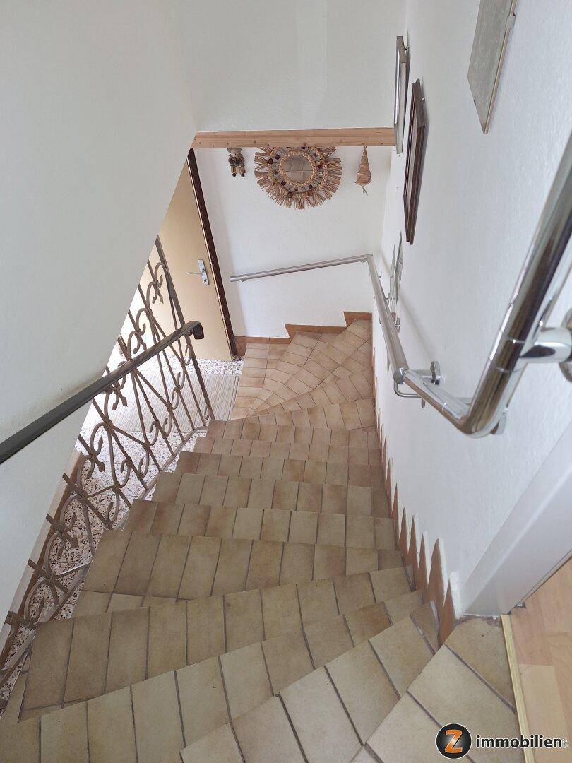 Blick von oben auf die geflieste Treppe mit Metallgeländer, die in den unteren Bereich führt.