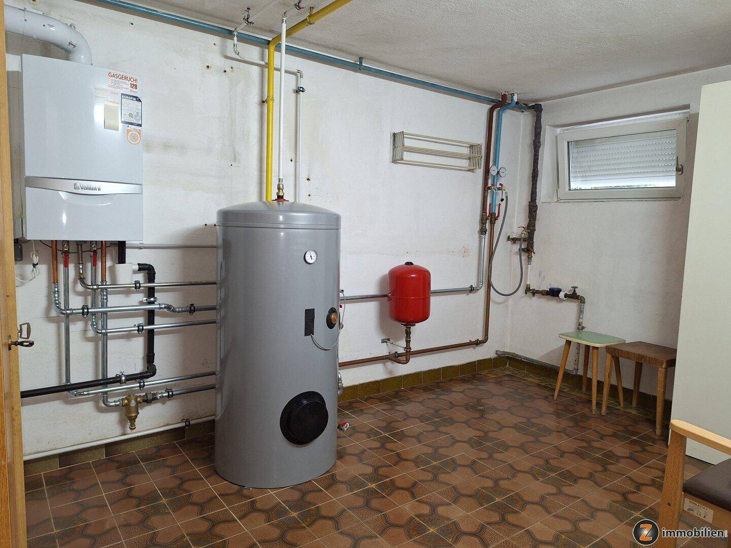 Heizungsraum im Keller mit Gastherme, Warmwasserspeicher und sichtbaren Rohrleitungen.