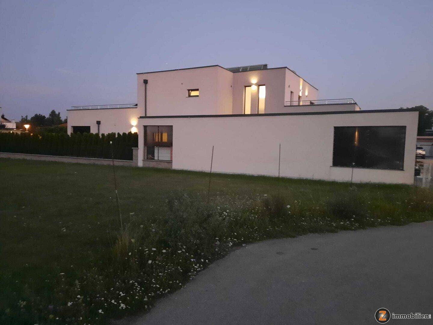 Modernes Wohnhaus bei Dämmerung mit minimalistischer Architektur und großzügiger Grünfläche.