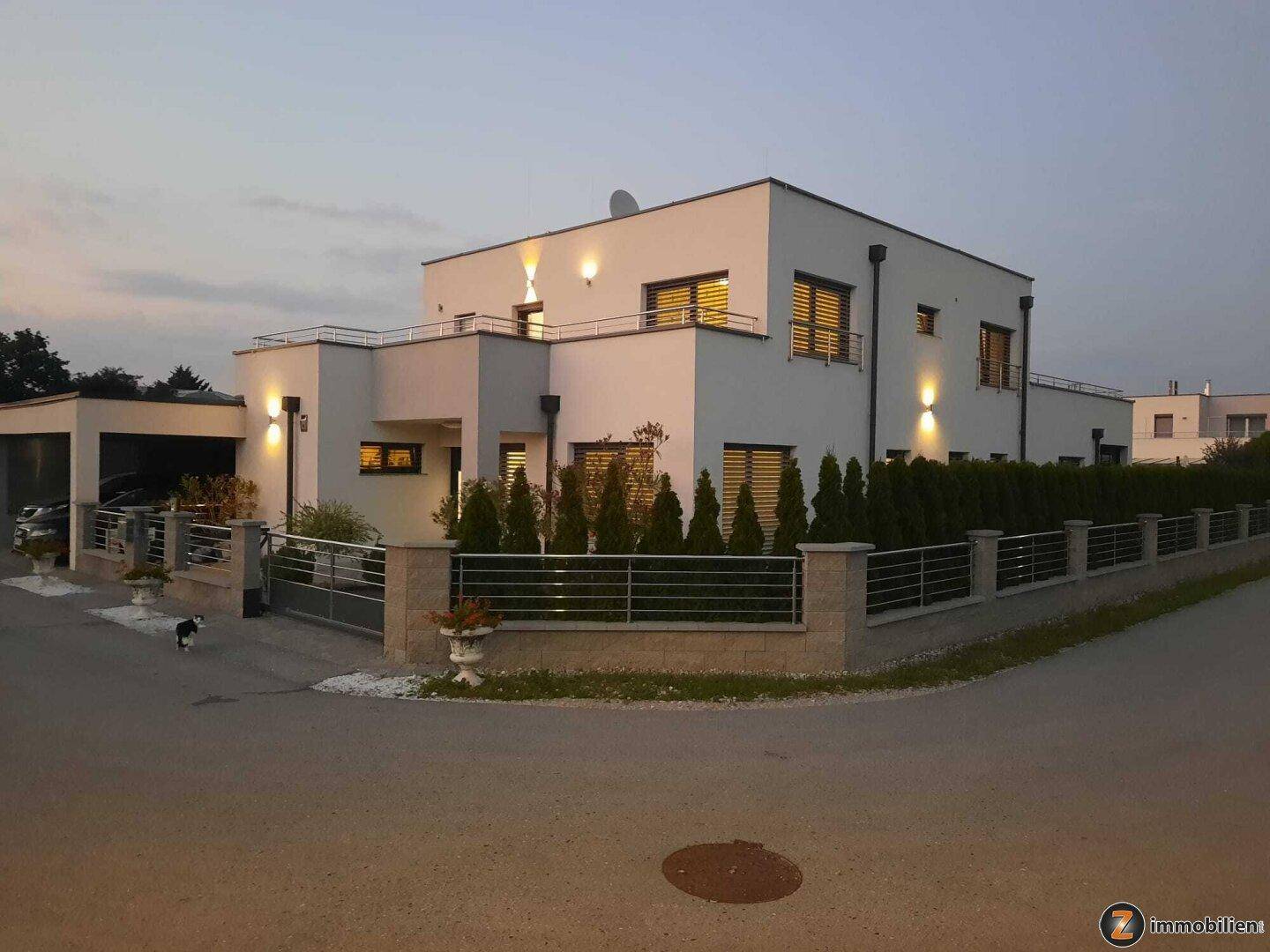 Modernes Wohnhaus mit Doppelgarage, umzäuntem Grundstück und stilvoller Außenbeleuchtung.