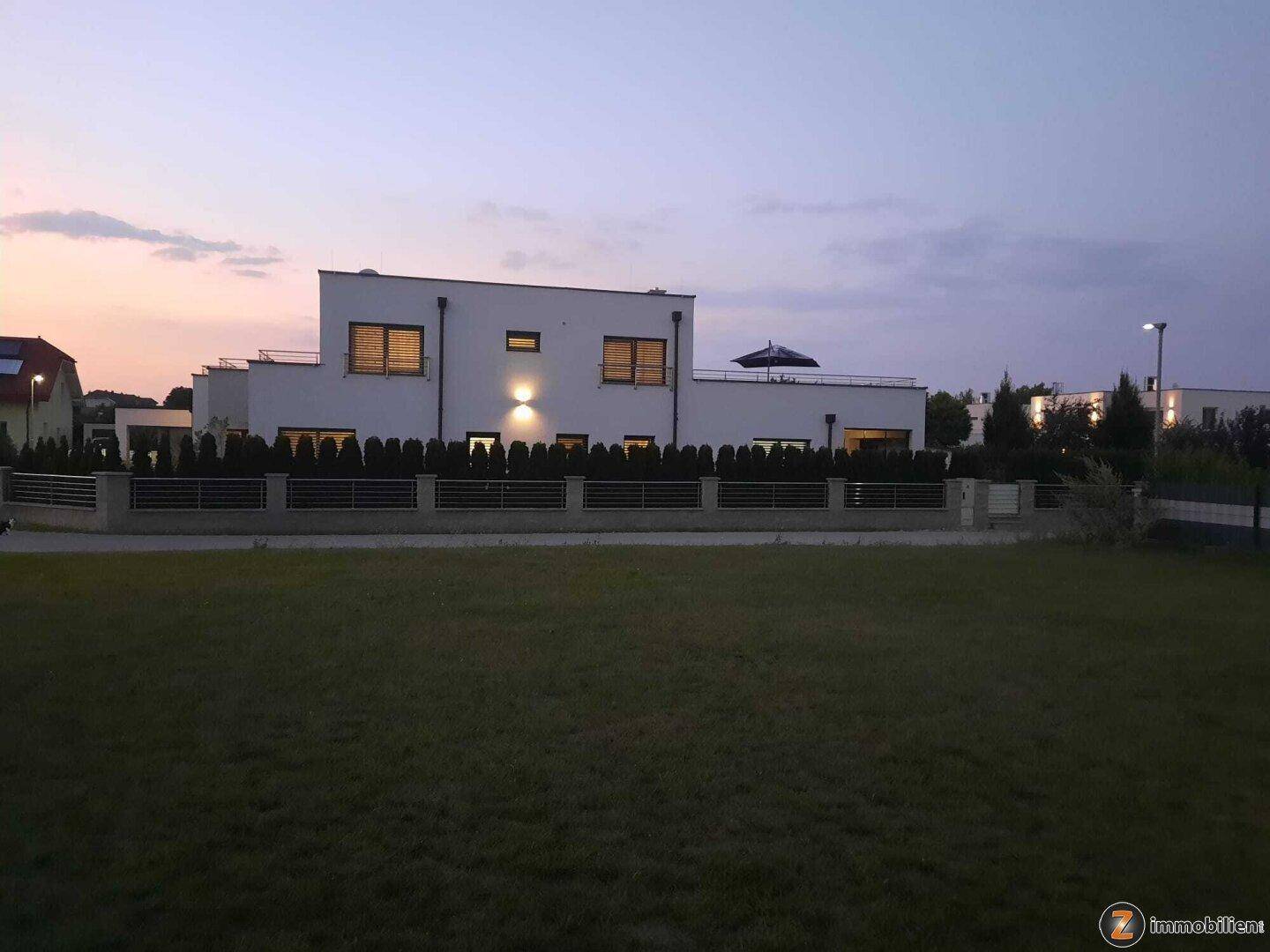 Elegantes Einfamilienhaus bei Sonnenuntergang mit gepflegtem Vorgarten und moderner Beleuchtung.