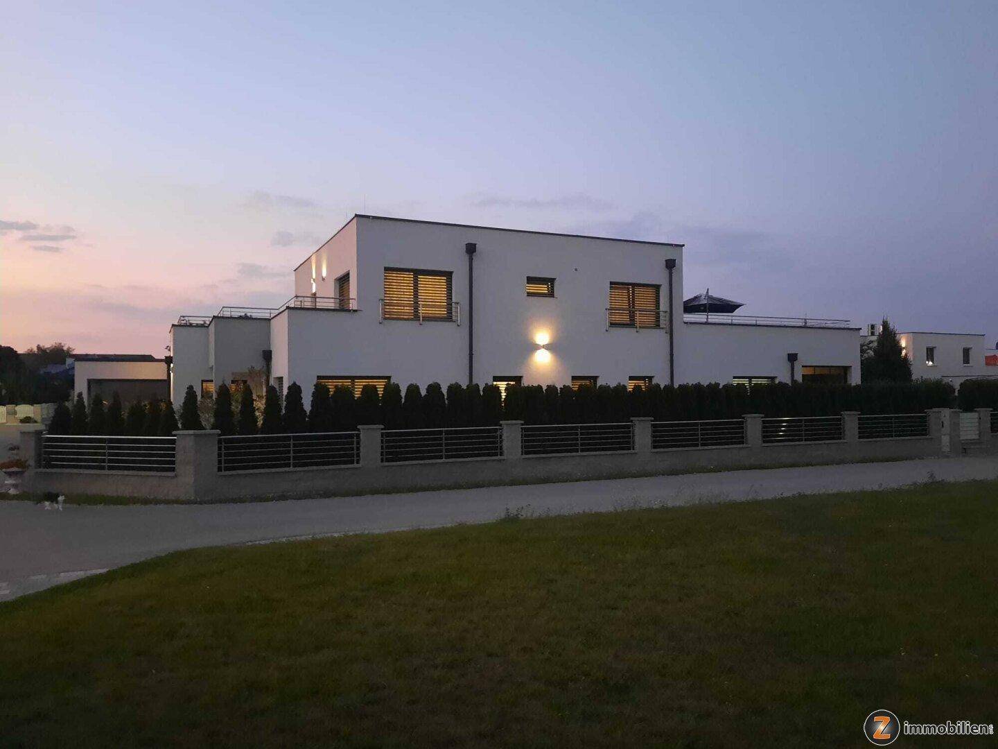 Modernes Wohnhaus bei Dämmerung mit gepflegter Hecke und stilvoller Außenbeleuchtung.