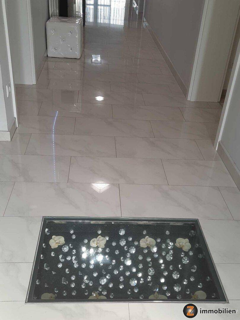 Heller Flur mit glänzenden Fliesen und dekorativem Bodenelement, das Licht reflektiert.