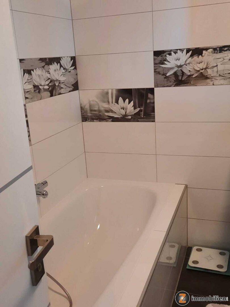 Modernes Badezimmer mit Badewanne und dekorativen Fliesen mit Seerosenmotiv.