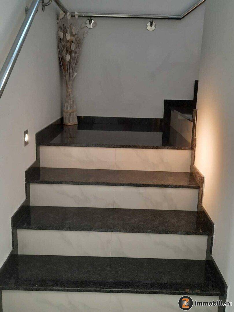 Treppenaufgang mit dunklen Granitstufen und hellem Marmor, ergänzt durch eine moderne Beleuchtung.