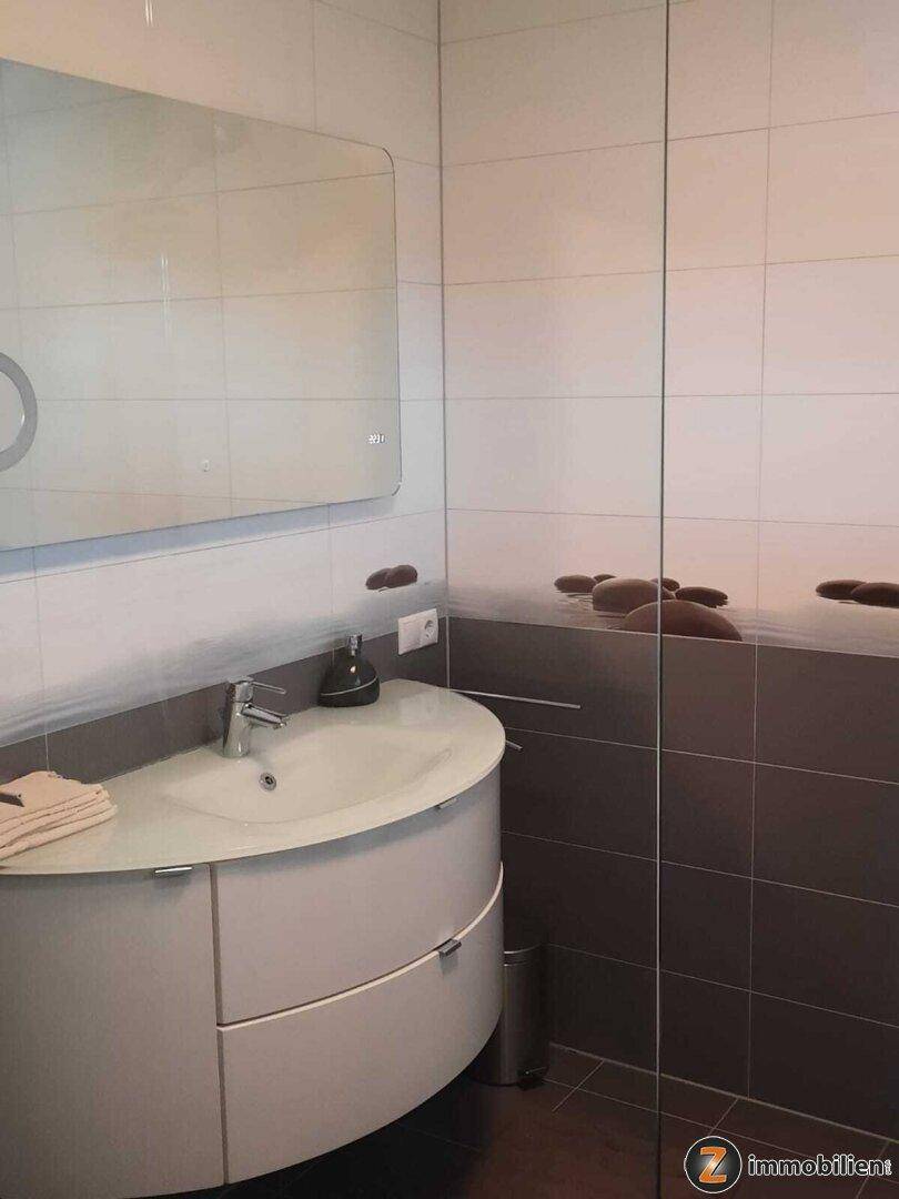 Modernes Badezimmer mit Einzelwaschbecken, großem Spiegel und stilvollen Fliesen.
