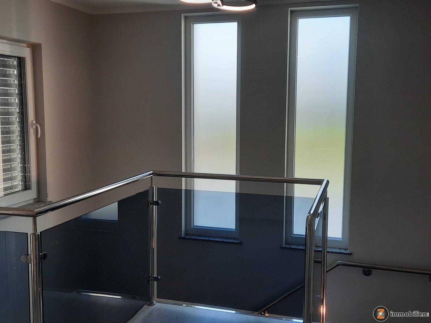 Moderner Treppenaufgang mit Glasgeländer und hohen, blickdichten Fenstern für Privatsphäre.