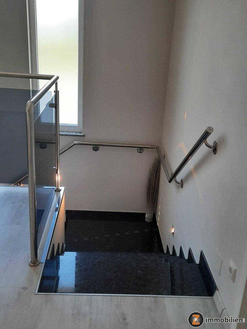 Eleganter Treppenabgang mit dunklen Granitstufen und einem schlichten Edelstahlhandlauf.