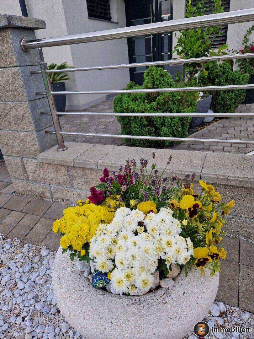 Dekorativer Blumenkübel mit bunten Blumen vor dem Hauseingang und einem modernen Geländer.