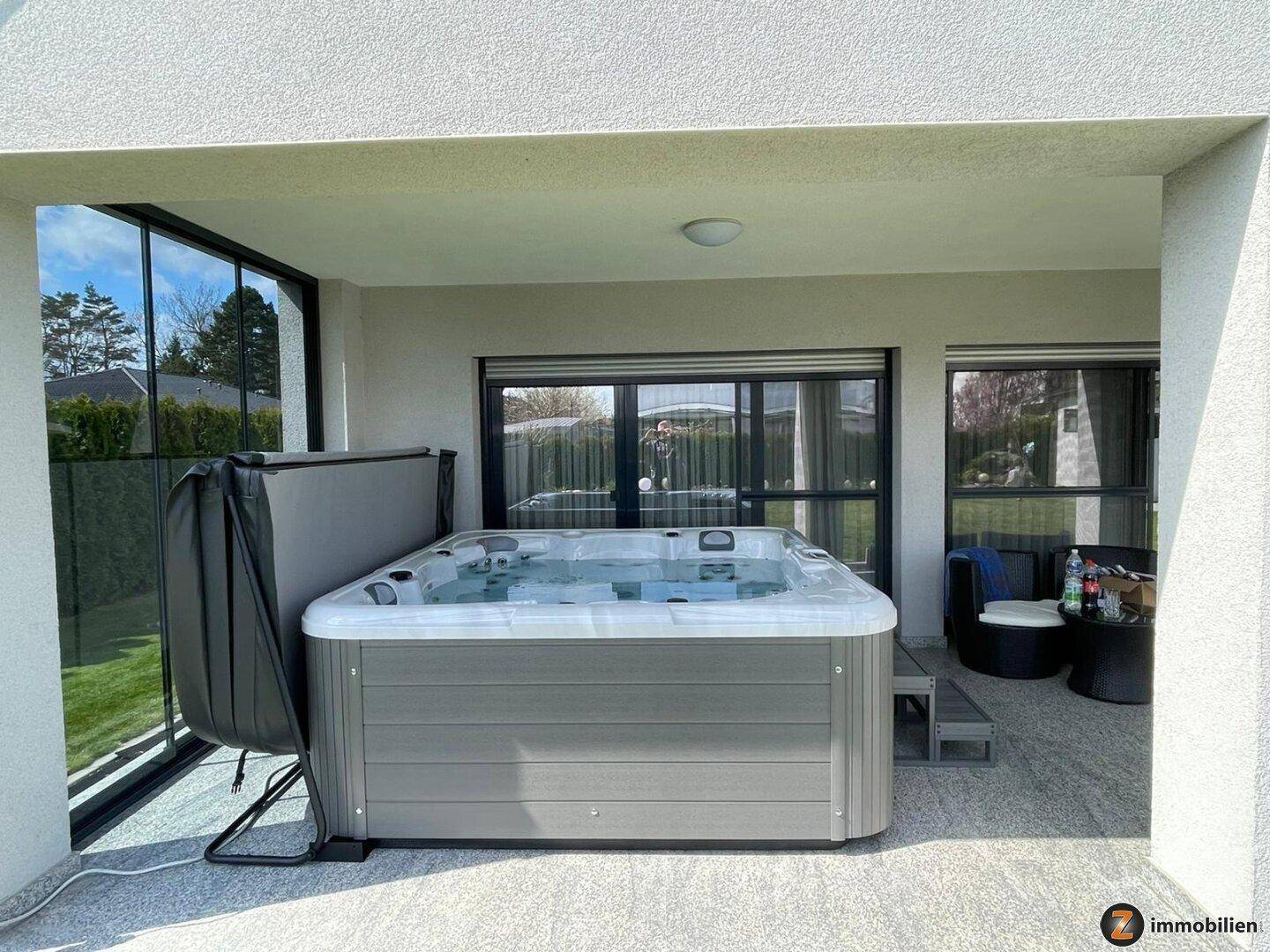 Überdachte Terrasse mit Whirlpool und Blick in den Garten, ideal für Wellness im Freien.