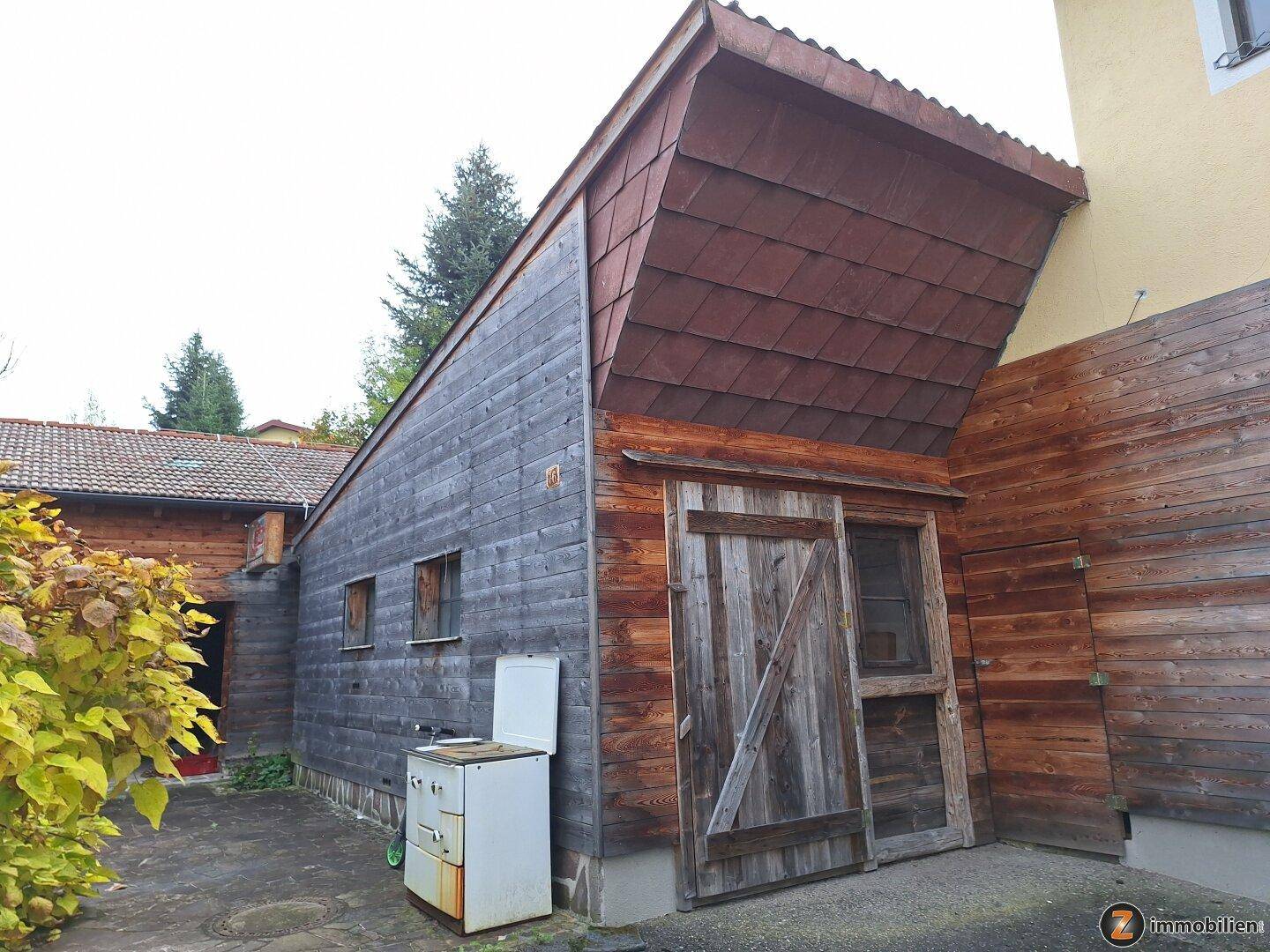 Rustikales Nebengebäude mit Holzverkleidung und einem großen Holztor, umgeben von Vegetation.