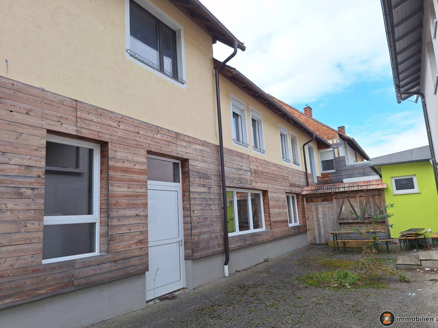 Seitenansicht des Gebäudes mit Holzverkleidung und einem schmalen Weg, der zum Hinterhof führt.