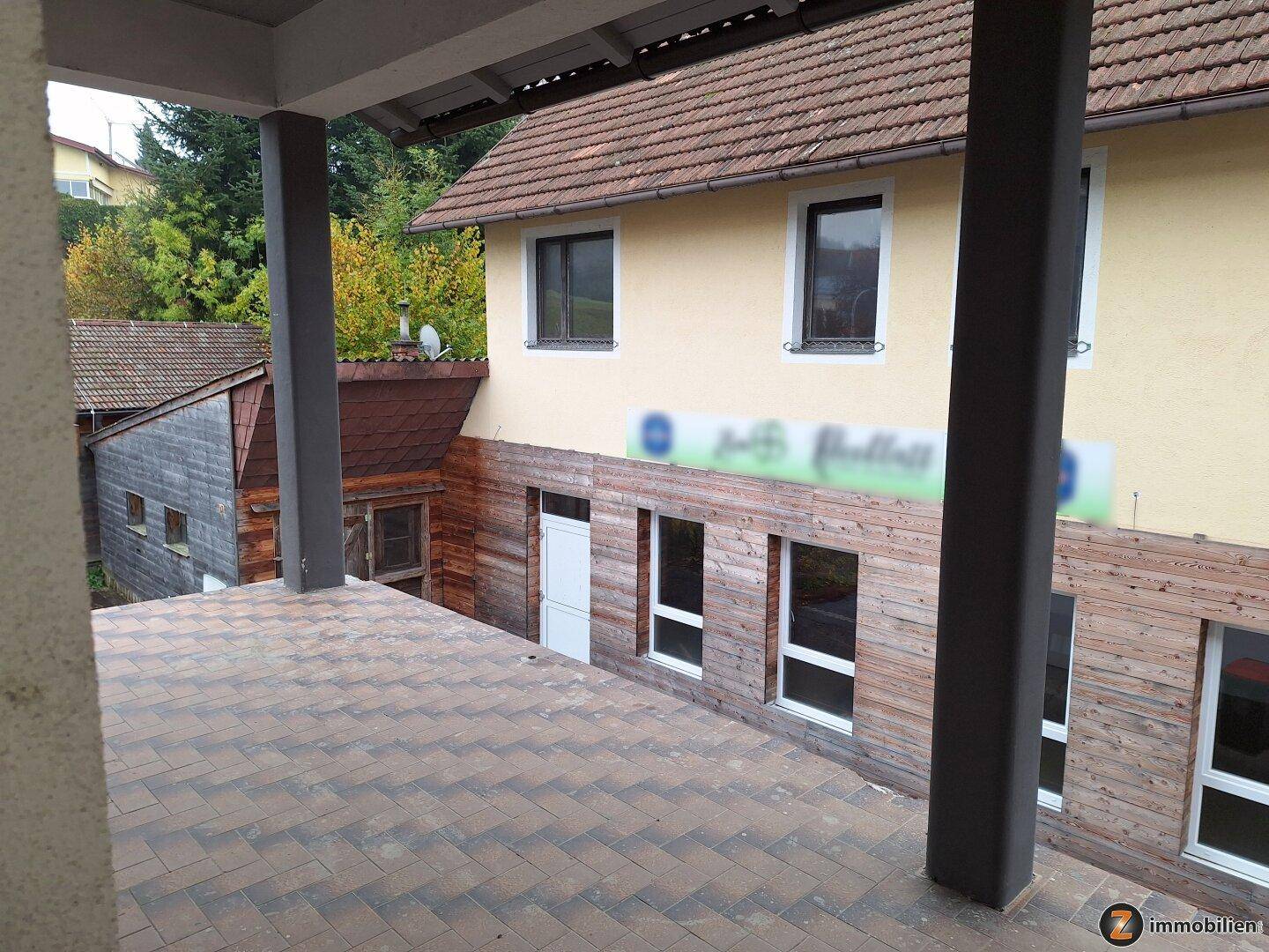 Überdachte Terrasse mit Fliesenboden und Holzsäulen, bietet einen Blick auf die umliegende Landschaft.