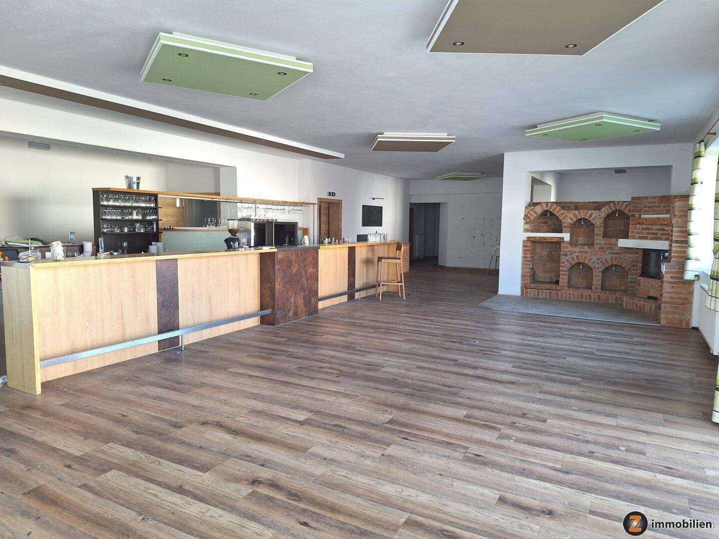 Großer offener Raum mit einer Bar, Holzboden und Deckenleuchten, ideal für Veranstaltungen.