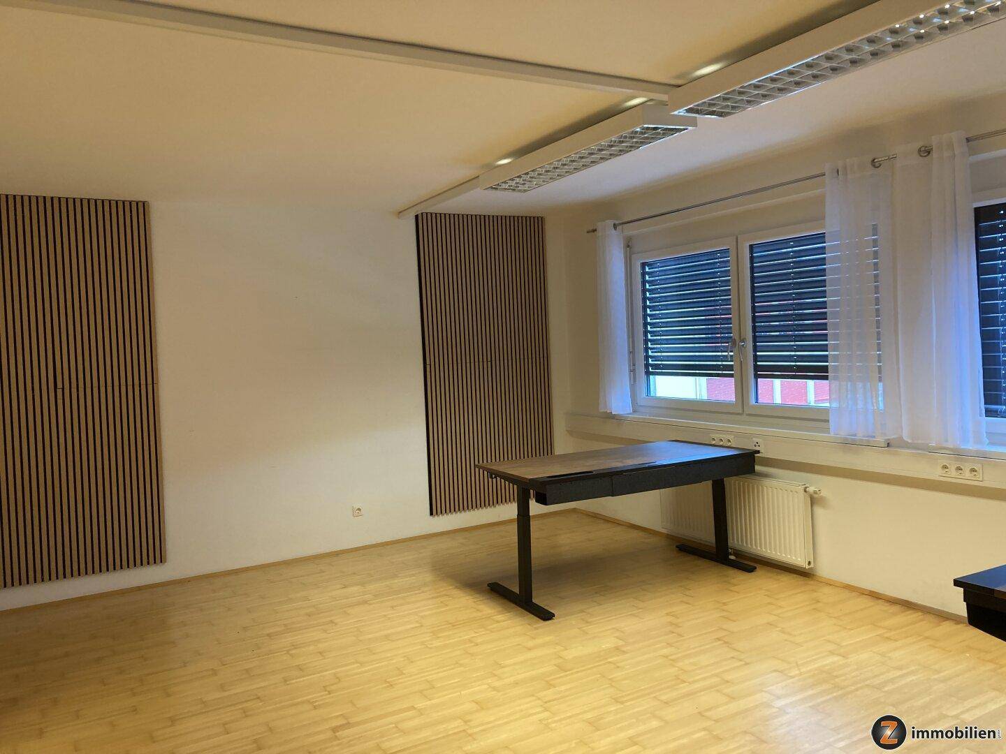 Geräumiger Büroraum mit Holzfußboden, vertikalen Holzpaneelen an der Wand und viel Tageslicht.