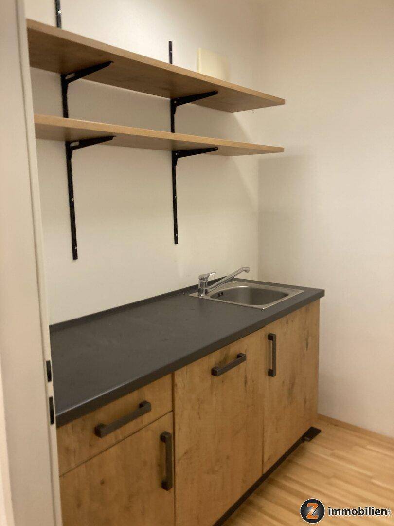 Kleine Küchenzeile mit Spülbecken, Unterschränken in Holzoptik und offenen Regalen.
