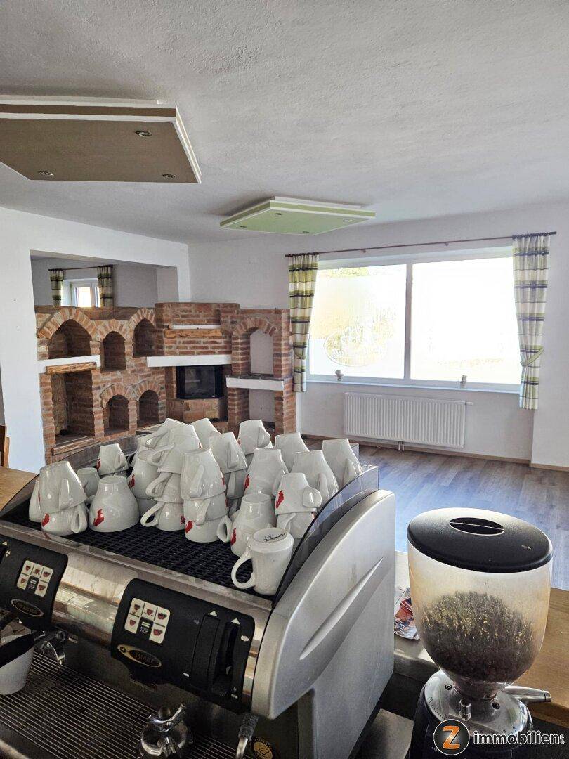 Geräumiges Wohnzimmer mit einem markanten gemauerten Kamin, großen Fenstern und einer professionellen Kaffeemaschine.