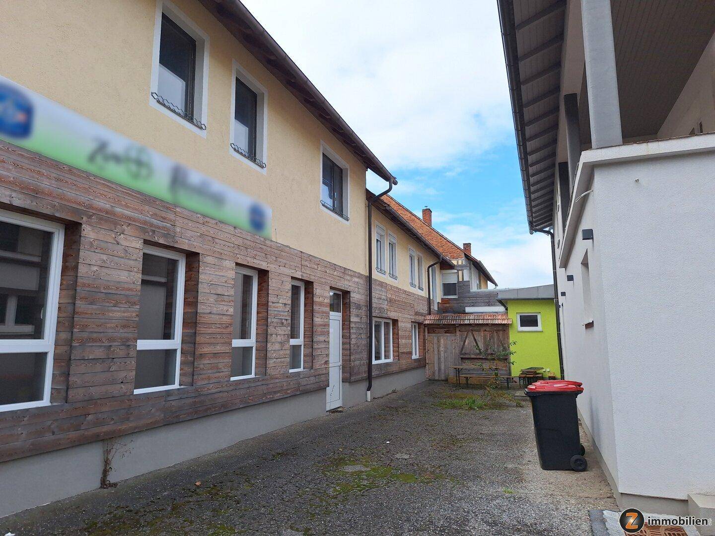Schmaler Durchgang zwischen zwei Gebäuden mit Holzakzenten und einem Mülleimer.