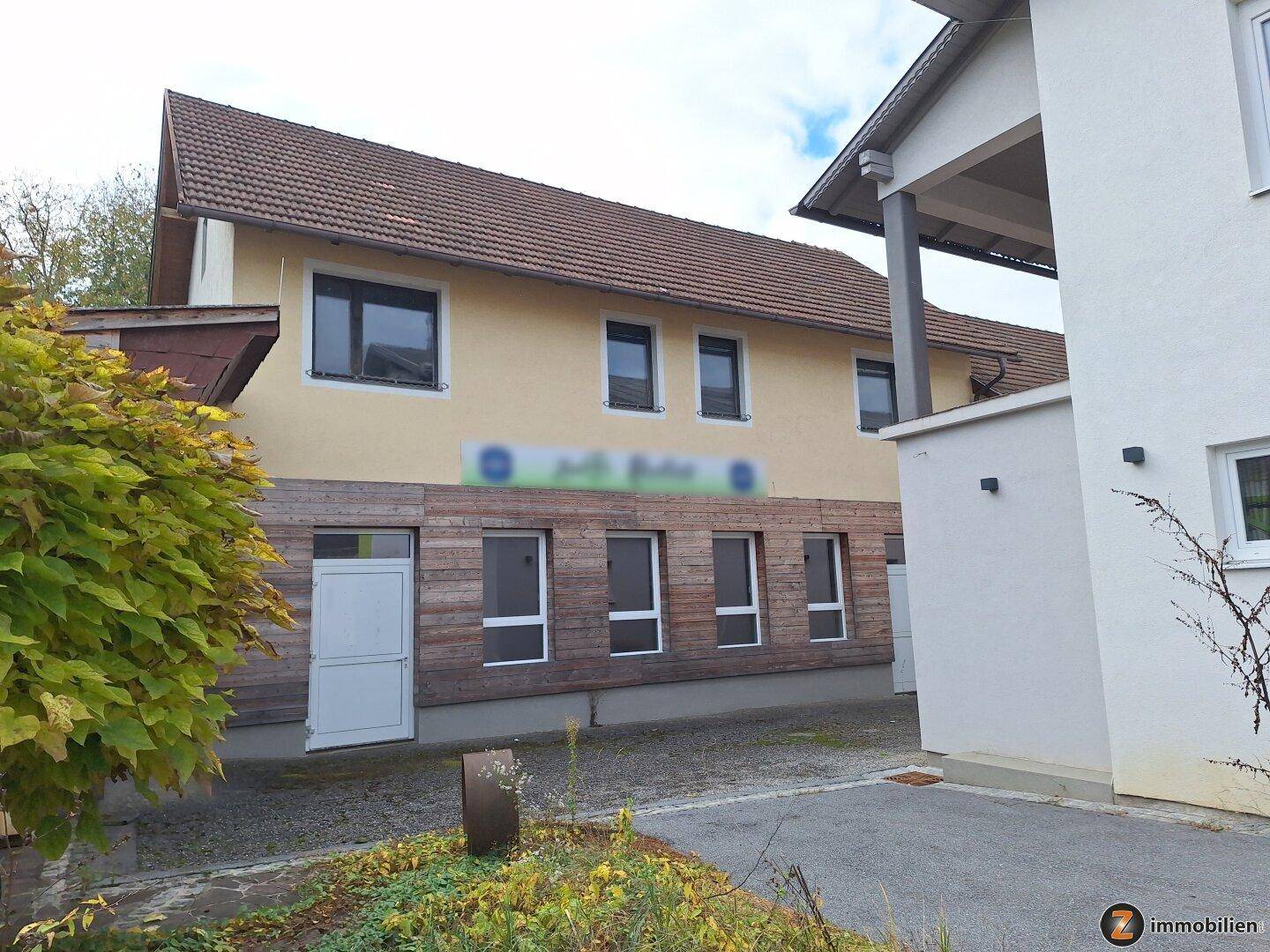 Rückansicht des Gebäudes mit Holzakzenten an der Fassade und einem gepflasterten Eingangsbereich.
