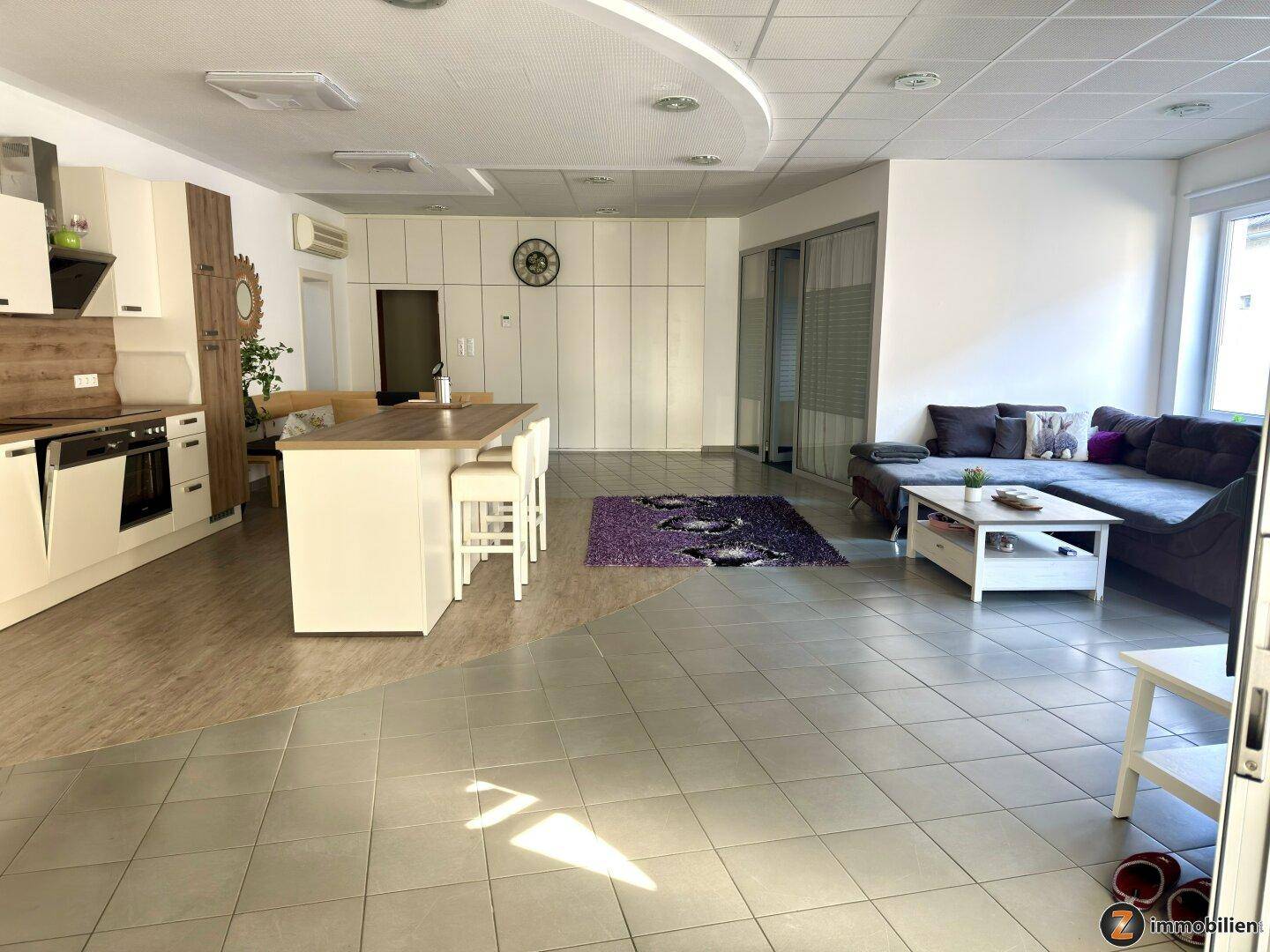 Geräumiger Wohn-Essbereich mit integrierter Küche, Sofa und modernem Fliesen- und Laminatboden.