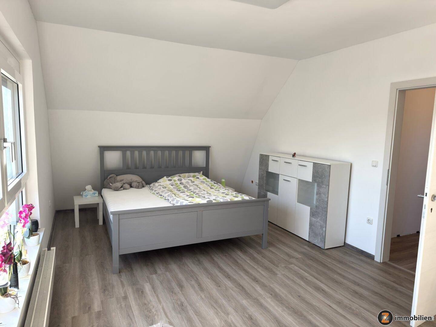 Helles Schlafzimmer im Dachgeschoss mit Laminatboden, Dachschräge und modernem Bett.