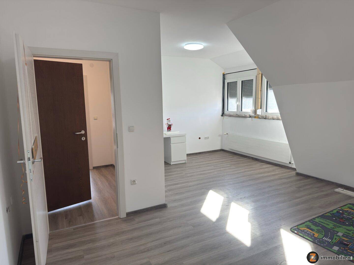 Heller Raum im Dachgeschoss mit Laminatboden, Dachschräge und Fenster, ideal als Schlaf- oder Arbeitszimmer.