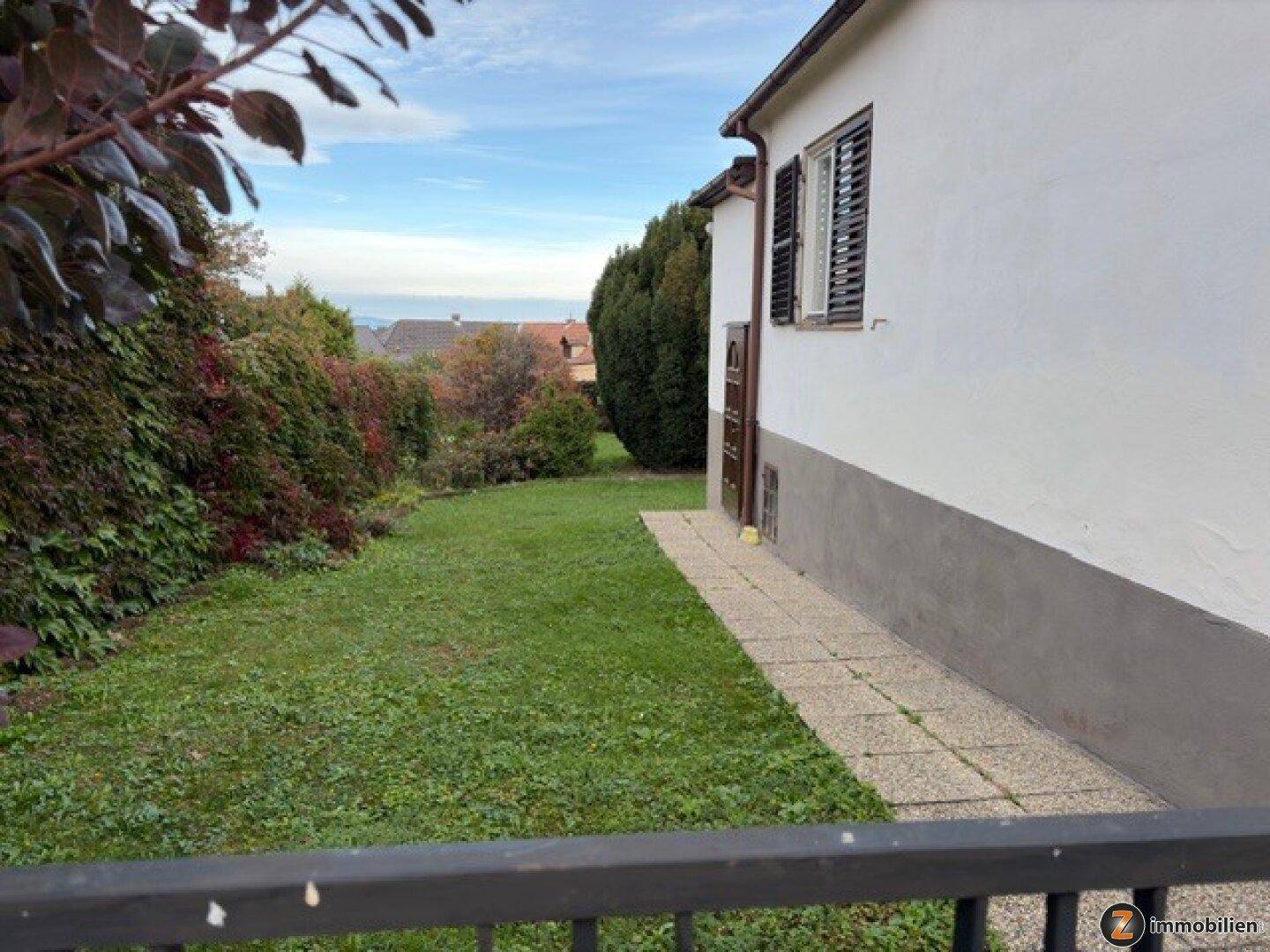 Seitlicher Gartenbereich mit Rasenfläche, Hecken und Blick auf die Umgebung.