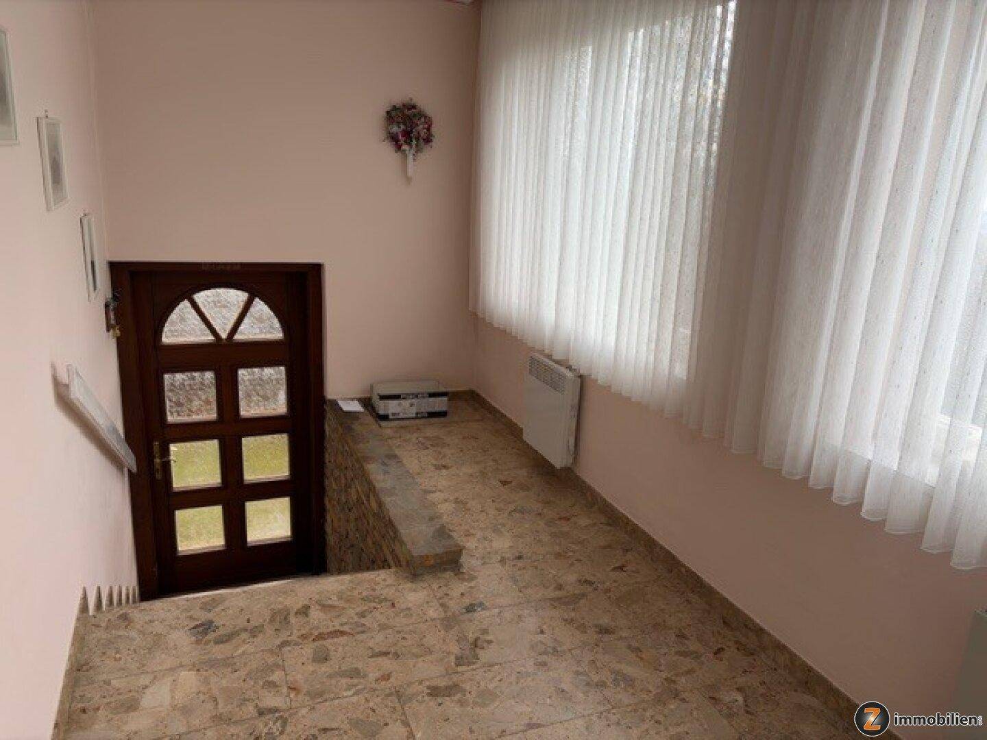 Heller Eingangsbereich mit gefliestem Boden, Treppe und Fenster mit Vorhängen.