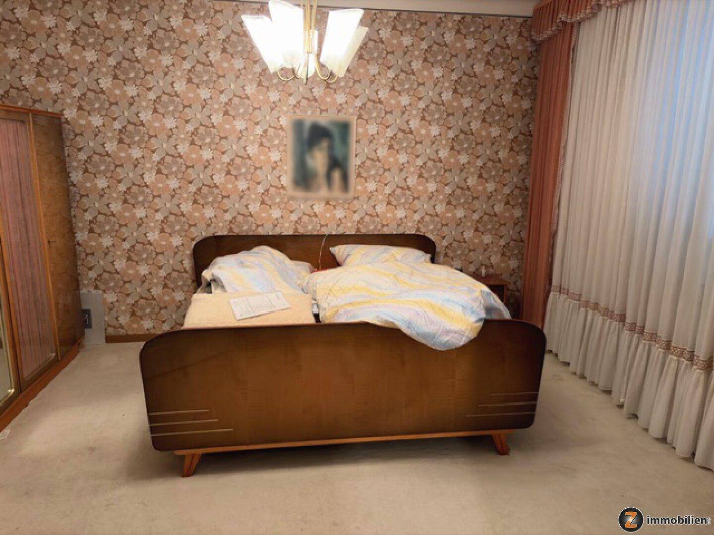 Schlafzimmer mit floraler Tapete, Doppelbett und klassischem Kleiderschrank.