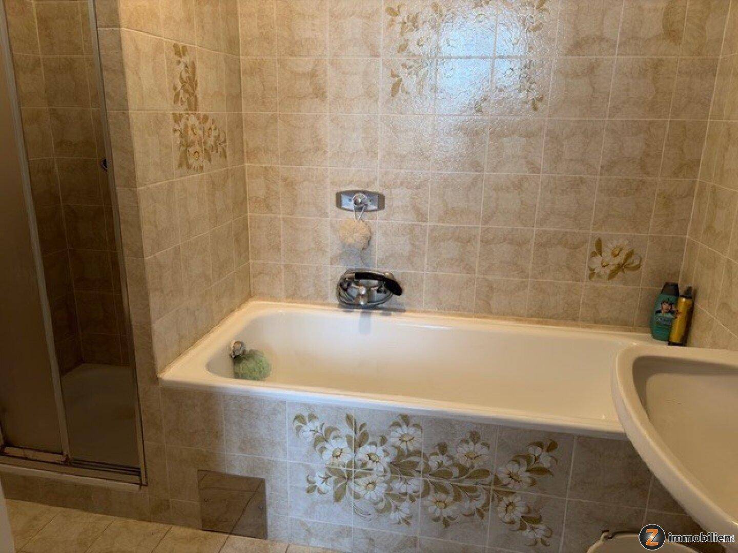 Badezimmer mit Badewanne, Duschkabine und beigen Fliesen mit Blumenmuster.